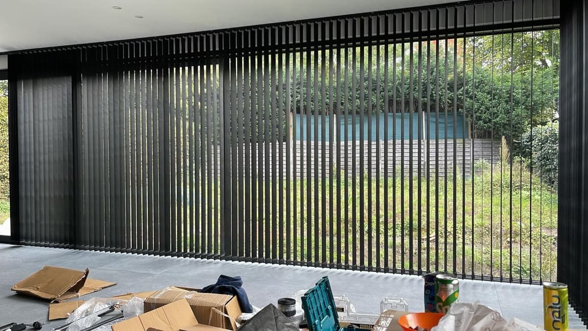 Zwarte verticale lamellen voor een raampartij met zicht op de tuin, tijdens de plaatsing - Sin-tex gordijnen en raamdecoratie, Heusden-Zolder