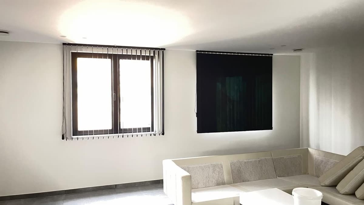 Donkere verticale lamellen voor een raam in een witte woonkamer - Sin-tex gordijnen en raamdecoratie, Heusden-Zolder